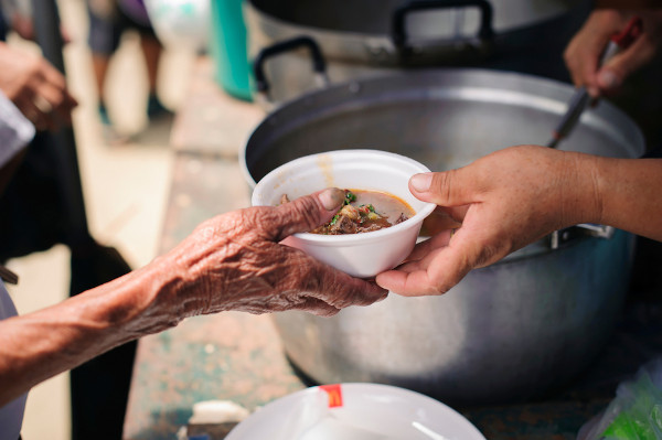 Marmita de sopa sendo passada de uma mão a outra, em gesto de caridade.