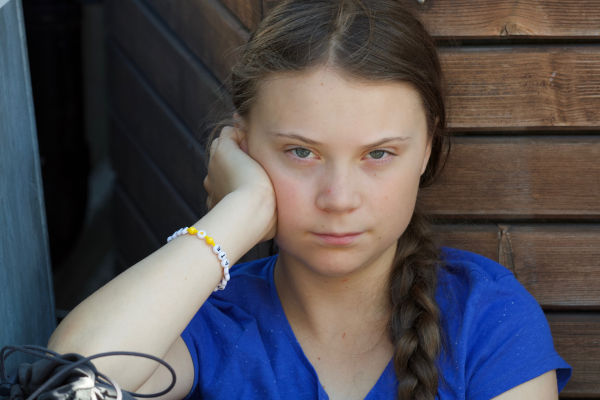Greta Thunberg com expressão séria e braço apoiando o rosto.