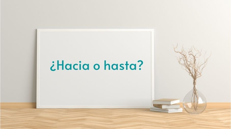 Uma tela branca, com o escrito “¿Hacia o hasta?”, ao lado de pequenos livros e de um objeto de decoração, sobre uma mesa de madeira.