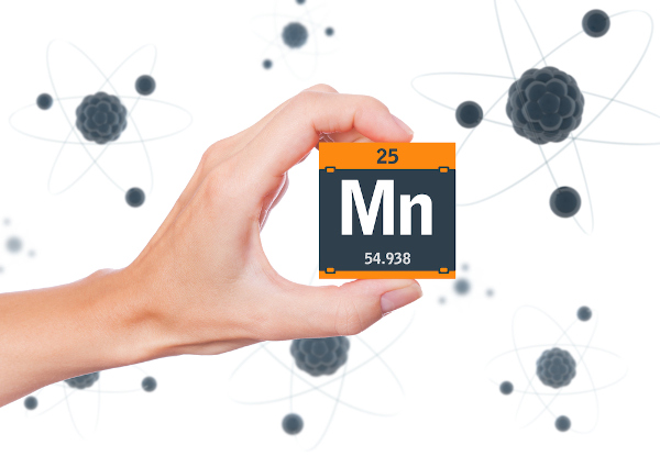 Pessoa segurando um cubo preto com laranja com o símbolo, o número atômico e a massa do elemento químico manganês.