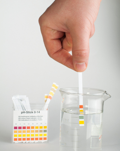 Pessoa testando o pH de um copo com água com uma fita de pH.