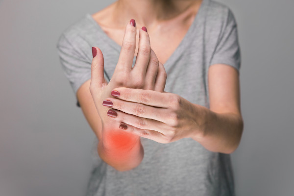 Jovem mulher segurando sua mão, com o punho sinalizado em vermelho, demonstrando sentir dor no local.