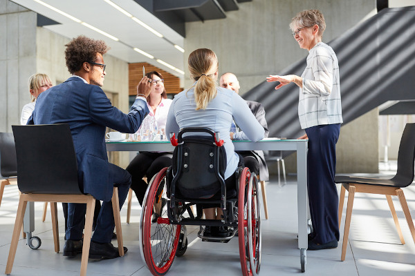 Mulher cadeirante participa de reunião de trabalho com demais colegas. 