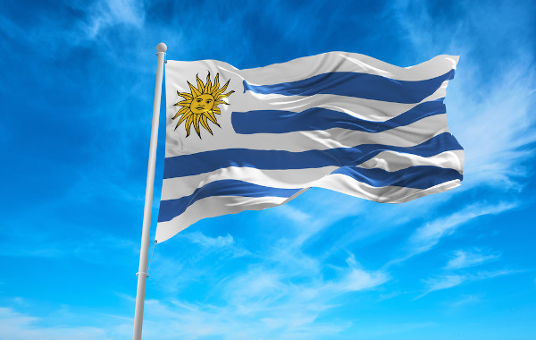 Bandeira do Uruguai hasteada e céu azul ao fundo.