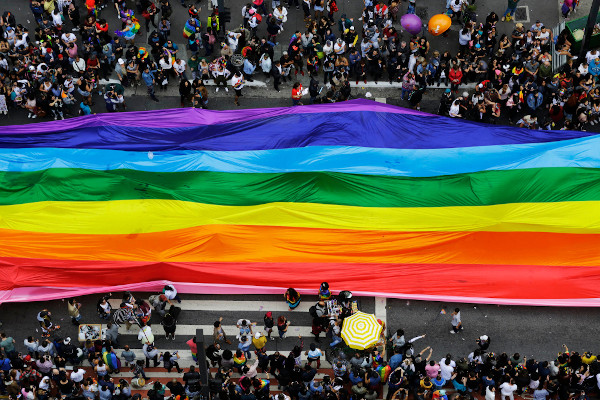 Pessoas seguram bandeira gigante com as cores do arco-íris e símbolo da comunidade LGBTQIA+ na Avenida Paulista, em São Paulo. [1]