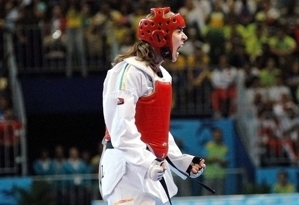 Atleta Natália Falavigna, com protetores na cor vermelha, comemora vitória após combate de taekwondo.
