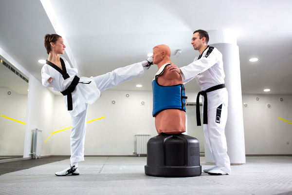 Atleta de cabelos curtos com deficiência física, sem os membros superiores, chuta boneco em treinamento de parataekwondo.