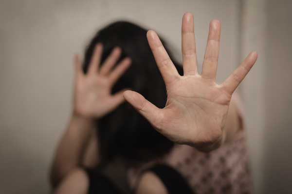 Imagem desfocada de uma mulher com as mãos levantadas em sinal de proteção em um contexto de violência contra a mulher.