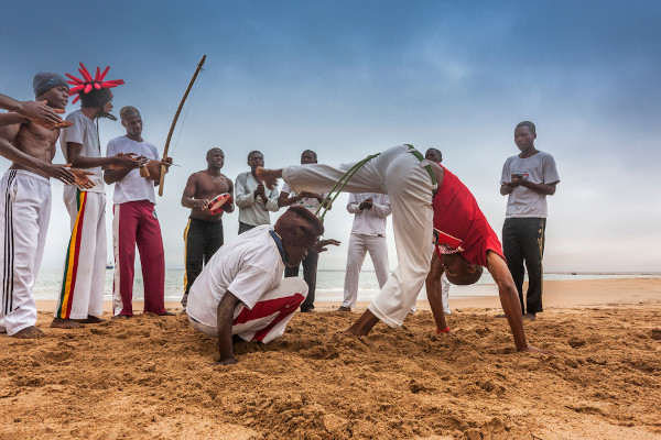 Dois homens lutando capoeira Angola em uma roda de capoeira na praia. 