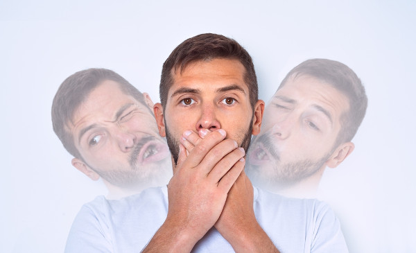 Homem com síndrome de Tourette fazendo caretas e cobrindo a boca com as mãos.