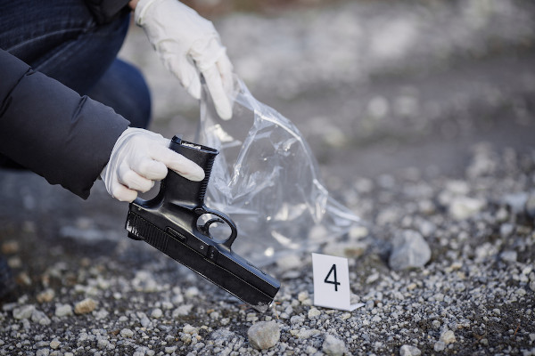 Investigação de cena de crime — perito, com luvas, coleta arma de fogo.