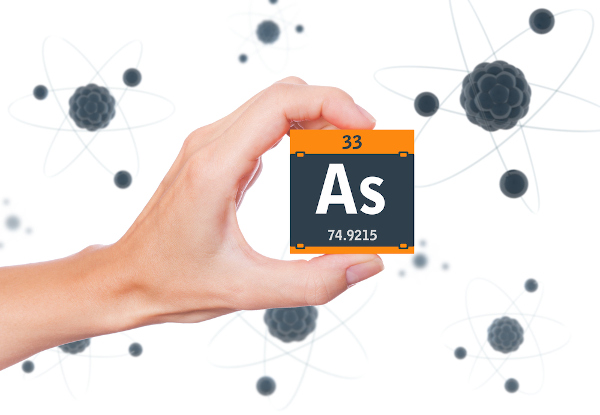Pessoa segurando um cubo preto com laranja com o símbolo, o número atômico e a massa do elemento químico arsênio.