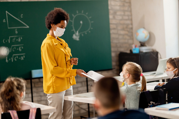 Professora com máscara de proteção em sala de aula cheia de alunos também com máscaras.