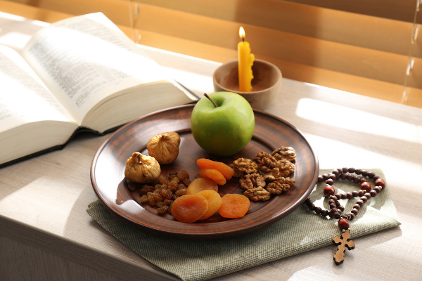 Prato com frutas e cereais, ao lado de um crucifixo, uma Bíblia e uma vela em cima de uma mesa, simbolizando a Quaresma.