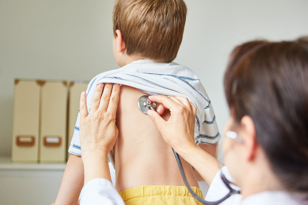 Médico examinando as costas de um menino com um estetoscópio; esse exame pode identificar o broncoespasmo.