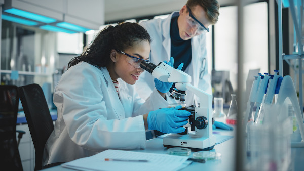 Dois cientistas em laboratório utilizando um microscópio, contexto que exemplifica o meio técnico-científico-informacional.