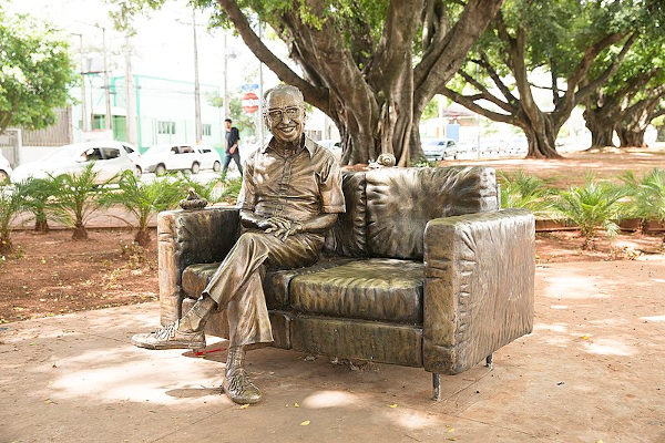 Escultura do poeta Manoel de Barros sentado em um sofá, em uma praça na cidade de Campo Grande.