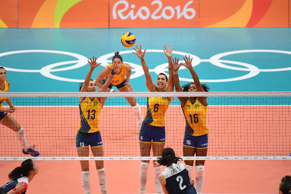 Mulheres da Seleção Brasileira de Vôlei fazem bloqueio em partida.