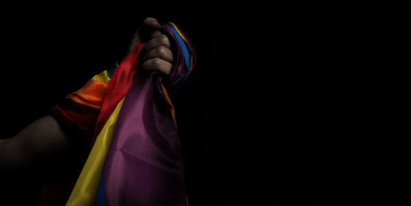 Mão de uma pessoa negra segurando a bandeira do arco-íris, um símbolo contra a discriminação.