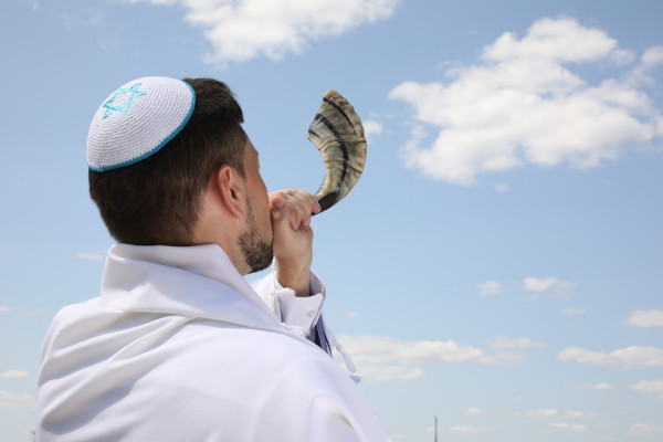 Judeu, com um quipá, tocando um shofar, outro importante símbolo do judaísmo.