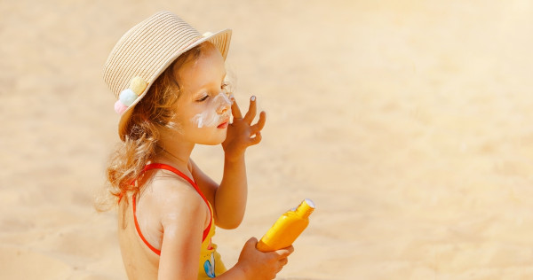 Criança passando protetor solar, produto que tem um fator de proteção solar (FPS), na praia.