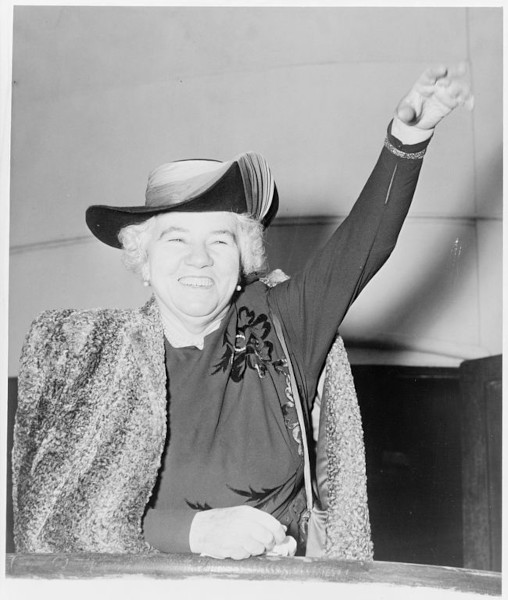 Fotografia em preto de branco de Elizabeth Kenny sorrindo e levantando o braço esquerdo.