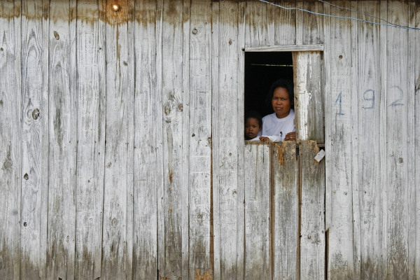Mãe e filho em janela de uma casa de madeira, em alusão à marginalização.
