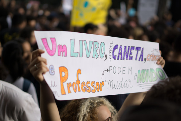 Cartaz com dizeres sobre educação nas mãos de uma mulher, em texto sobre educação no Brasil