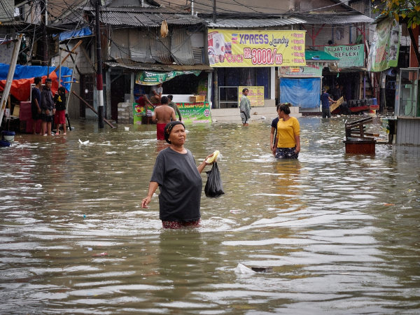 Pessoas andando pelas ruas da cidade em um contexto de inundação, com água próximo ao quadril.