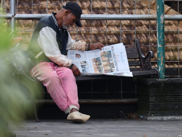 Idoso lendo jornal em uma praça, em texto sobre analfabetismo funcional.