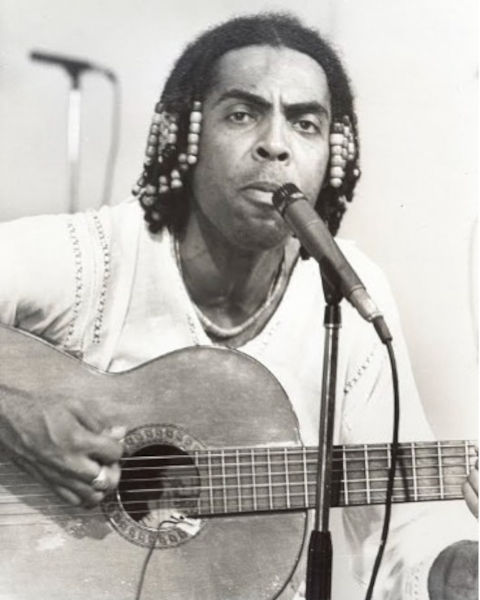 Foto preto e branco de Gilberto Gil tocando violão e próximo a microfone.