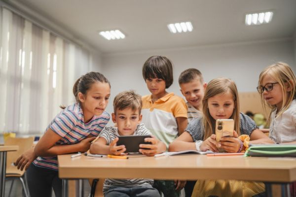 Crianças mexendo no celular em alusão às leis que restringe o uso dos celulares dentro das escolas.