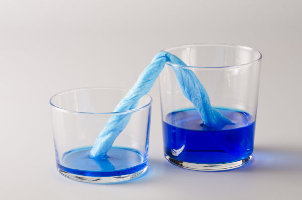 Dois copos com líquido azul e um papel entre eles transportando o líquido por meio da capilaridade. Dois copos com líquido azul e um papel entre eles transportando o líquido por meio da capilaridade.