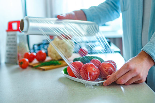 Pessoa embalando tomates e pepinos com insulfilme feito com polipropileno (PP).