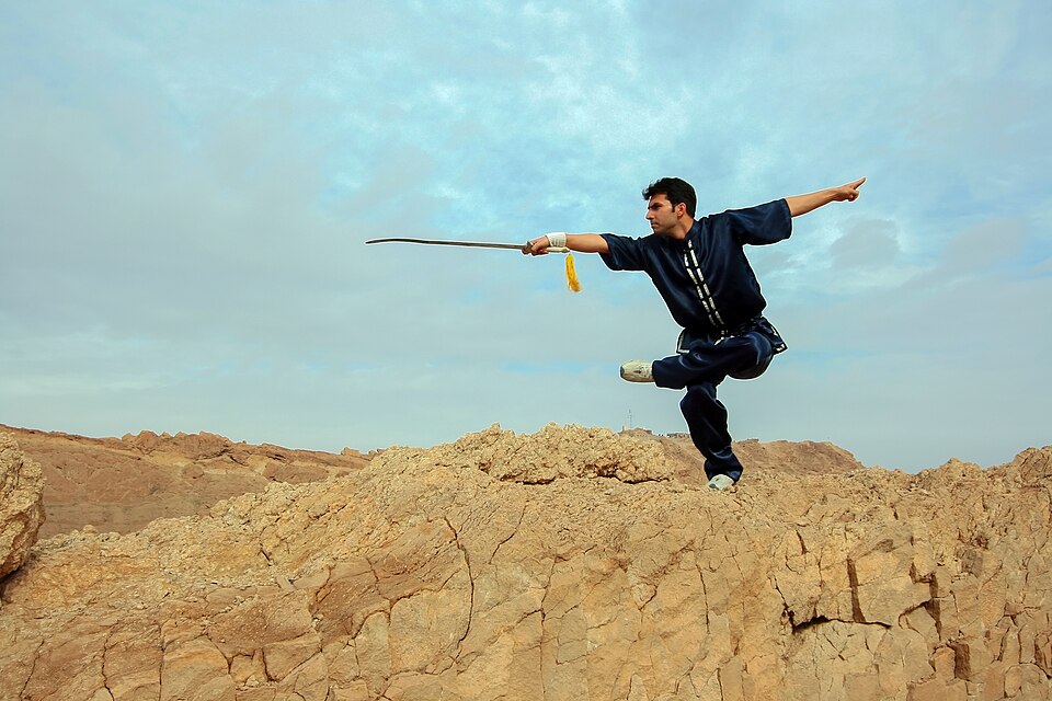 Praticante faz movimento estático e segura arma de kung fu.