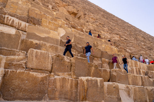 Turistas caminham sobre blocos de calcário que formam as pirâmides do Egito.