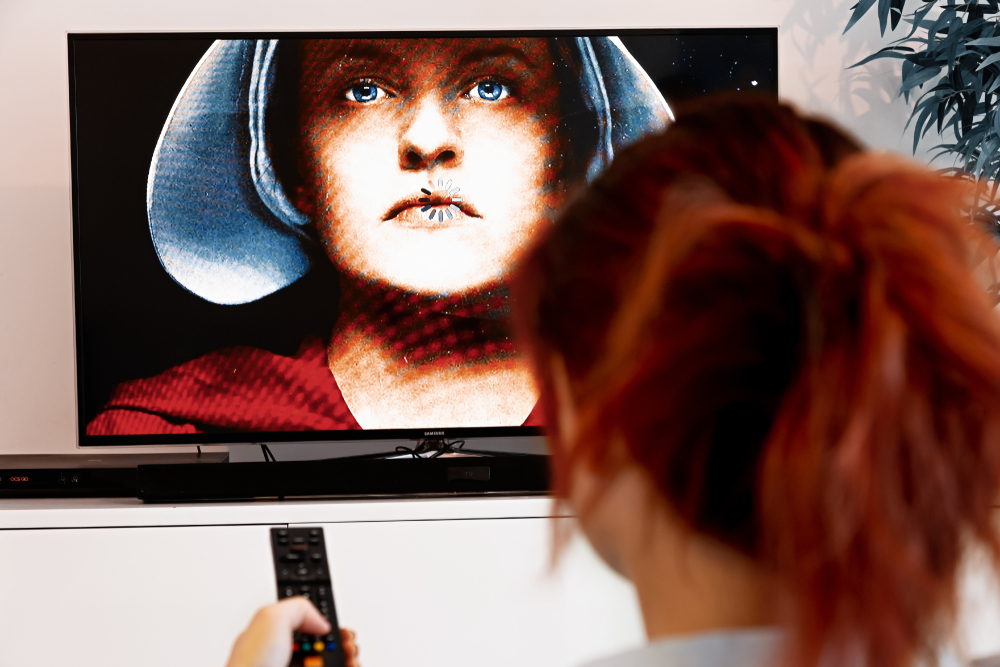 Mulher assistindo à série “O conto da aia”, série lançada em 2017 e inspirada no livro de Margaret Atwood.
