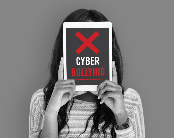 Menina com um tablet em frente ao rosto com o escrito "cyberbullying".