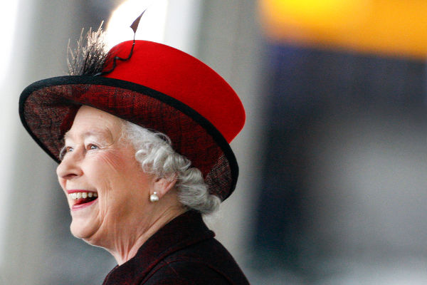 Rainha Elizabeth II aparece em foto de perfil sorrindo com chapéu vermelho com preto