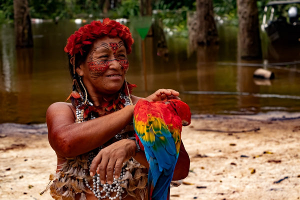Mulher indígena com pinturas faciais e com arara vermelha, amarela e azul nos braços