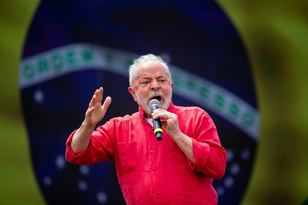 Homem idoso branco de camisa vermelha com bandeira do Brasil ao fundo