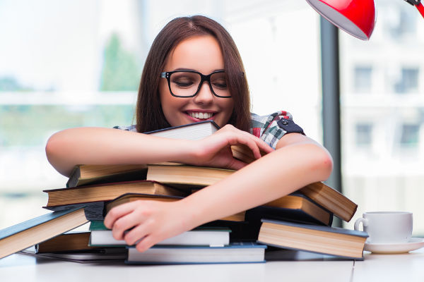 estudante sorridente usando óculos abraçando livros