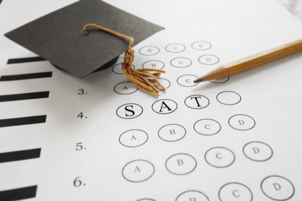 Lápis e chapéu de formatura sobre um gabarito com o texto SAT
